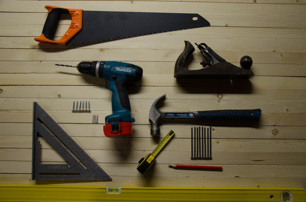 Assorted hand tools laid out deliberately on a wooden surface, including a saw, drill, plane, and tape measure